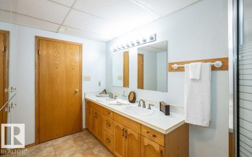 Dual vanity with integrated sinks, wood-finish cabinetry, and a large wall-mounted mirror - 11007 108 Avenue, Westlock, AB 