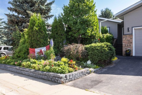 Front exterior featuring gray siding, a gray garage door, brick accenting, and a landscaped garden bed with a stone retaining wall - 11007 108 Avenue, Westlock, AB 