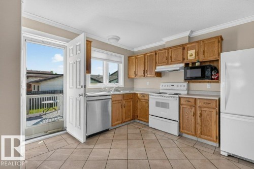 Kitchen featuring wood cabinetry, white appliances, tile flooring, and a stainless steel dishwasher - 14527 32 Street Nw, Edmonton, AB 