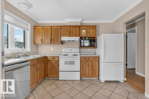 Kitchen with wood cabinetry, white appliances, stainless steel sink, and tile flooring - 14527 32 Street Nw, Edmonton, AB 