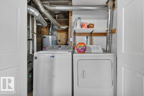 Dedicated laundry room featuring side-by-side washer and dryer appliances, wooden shelving with storage capacity, metal ductwork, and white finished walls with recessed lighting - 14527 32 Street Nw, Edmonton, AB 