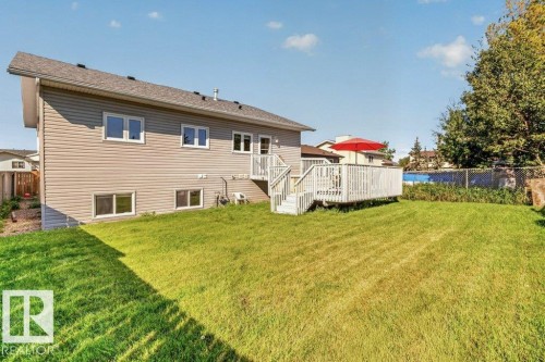 Expansive backyard featuring a manicured lawn, a large wooden deck with railing, and mature trees - 14527 32 Street Nw, Edmonton, AB 