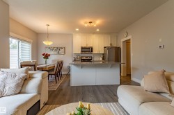 Open-concept interior featuring wood-finish flooring, a kitchen island with seating, stainless steel appliances, white cabinetry, and a dining area with a sliding glass door - 