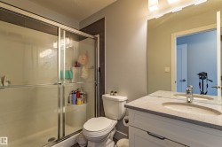 Bathroom featuring a glass-enclosed shower with integrated shelving, a single vanity with a stone-finish countertop, and a large wall-mounted mirror with overhead lighting - 