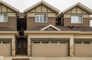 Multi-level townhome exterior featuring an attached garage, complementary siding, stone accents, and a shingled roof - #14 4835 Wright Dr Sw Sw, Edmonton, AB  - Outdoor With Facade 