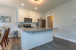 Kitchen featuring white shaker-style cabinetry, stainless steel appliances, subway tile backsplash, and a central island with a light-toned countertop - 