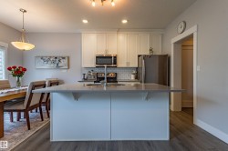 Modern kitchen featuring an island with a light-toned countertop, stainless steel appliances, white cabinetry with silver hardware, and a subway tile backsplash - 