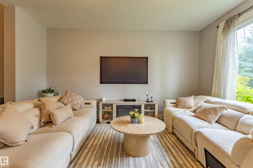 Spacious room featuring light-toned walls, wood-finish flooring with a patterned area rug, and a large window with sheer drapes - #14 4835 Wright Dr Sw Sw, Edmonton, AB - Indoor Photo Showing Living Room