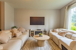 Spacious room featuring light-toned walls, wood-finish flooring with a patterned area rug, and a large window with sheer drapes - 