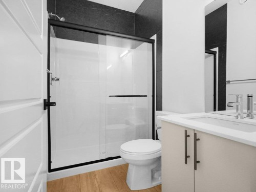 Black-framed sliding shower door, white tiled shower, black large format wall tile, wood-finish flooring, and a vanity with a rectangular basin - 912 17 Ave Nw, Edmonton, AB 