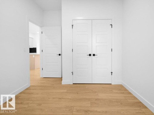 Light wood-finish flooring, white paneled doors, black hardware accents, and bright white walls - 912 17 Ave Nw, Edmonton, AB 