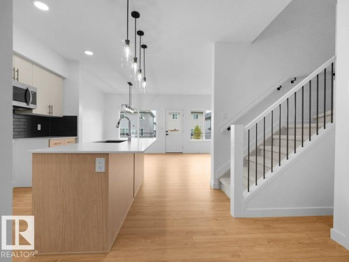 Open-concept kitchen with wood-finish flooring, island with white countertop, recessed lighting, and stainless steel appliances - 912 17 Ave Nw, Edmonton, AB 