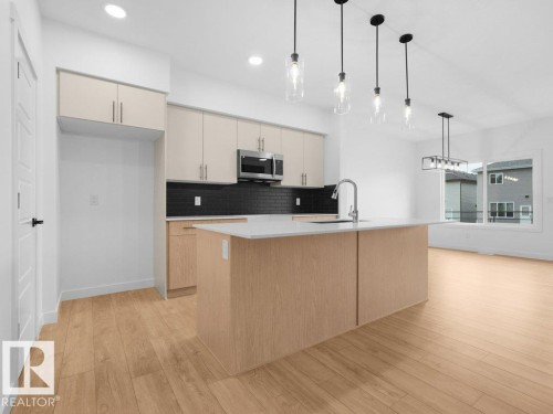 Open concept kitchen featuring an island with an integrated sink, stainless steel microwave, black subway tile backsplash, and wood-finish flooring - 912 17 Ave Nw, Edmonton, AB 