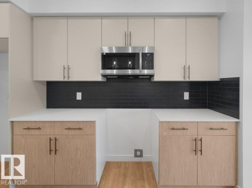 Sleek kitchen featuring light-toned upper cabinetry, stainless steel microwave, black subway tile backsplash, white countertops, and wood-finish lower cabinetry - 912 17 Ave Nw, Edmonton, AB 
