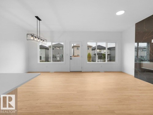 Wood-finish flooring throughout, multiple windows, contemporary linear chandelier, recessed ceiling lighting, and a dark stone-finish accent wall - 912 17 Ave Nw, Edmonton, AB 