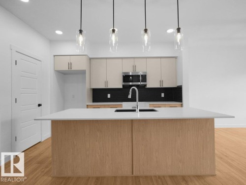 Kitchen island with a white countertop and integrated sink, pendant lighting fixtures, stainless steel appliances, two-tone cabinetry, and wood-finish flooring - 912 17 Ave Nw, Edmonton, AB 