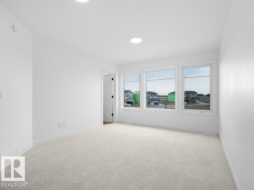 Neutral carpet flooring, white walls, three large windows, recessed lighting, and a solid interior door - 912 17 Ave Nw, Edmonton, AB 
