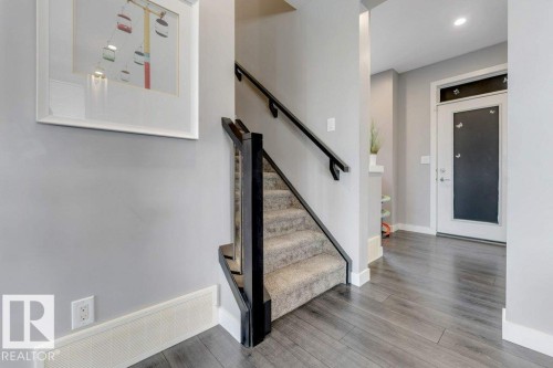 Carpeted staircase with dark wood-finish railing, wood-finish flooring, and a white entry door with frosted glass panel - #45 16903 68 St Nw, Edmonton, AB 