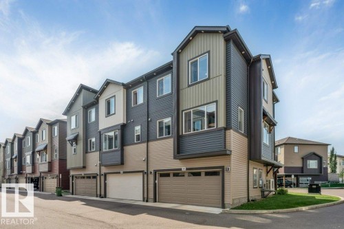 Modern townhouse exterior featuring multi-toned siding, prominent bay windows, and attached garages with sectional doors - #45 16903 68 St Nw, Edmonton, AB 