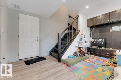 Wood-finish flooring, staircase with dark wood treads and banister, built-in shelving, built-in cabinetry, and white paneled door - #45 16903 68 St Nw, Edmonton, AB 