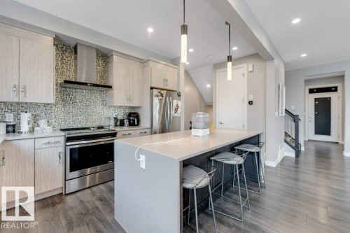 Kitchen featuring light wood-finish cabinetry, stainless steel appliances, a tiled backsplash, a kitchen island with a light countertop, and recessed lighting - #45 16903 68 St Nw, Edmonton, AB 