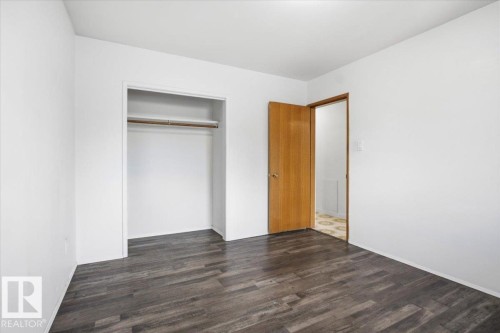 Wood-finish flooring, white walls, wood interior door, and a built-in closet with hanging rod - 13235 82 Street Nw, Edmonton, AB 