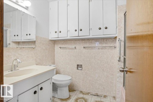 Vanity with integrated sink, wall-mounted medicine cabinet, extensive upper cabinetry, tiled walls, and patterned floor tiles - 13235 82 Street Nw, Edmonton, AB 
