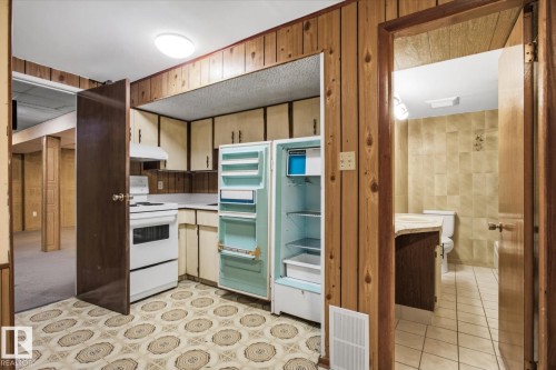 Kitchenette featuring wood paneling, white appliances, and patterned floor tile - 13235 82 Street Nw, Edmonton, AB 