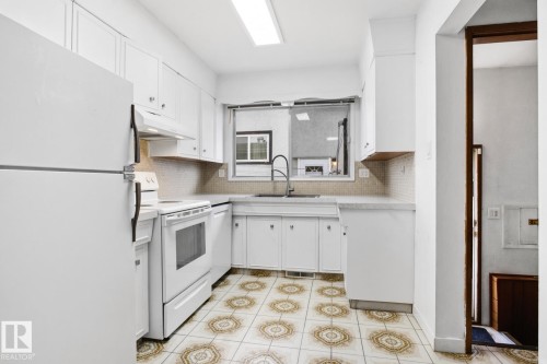 Kitchen featuring white cabinetry, a tile backsplash, a window above the sink, a built-in range, and patterned floor tiling - 13235 82 Street Nw, Edmonton, AB 