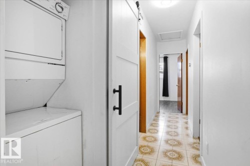 Stackable laundry appliances, white panel barn door, matte black hardware, tile flooring with circular patterns, and a flush-mount ceiling light - 13235 82 Street Nw, Edmonton, AB 