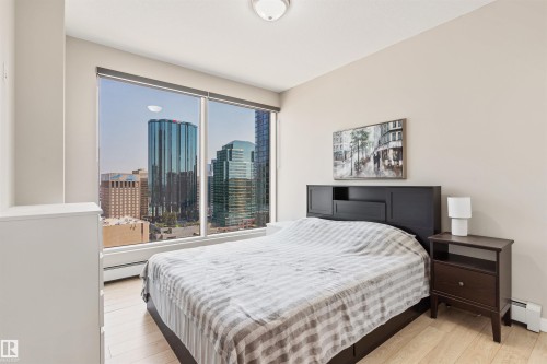 Bedroom featuring expansive windows with cityscape scenery, light wood-finish flooring, and a built-in baseboard heater - #2205 10226 104 St Nw, Edmonton, AB - Indoor Photo Showing Bedroom