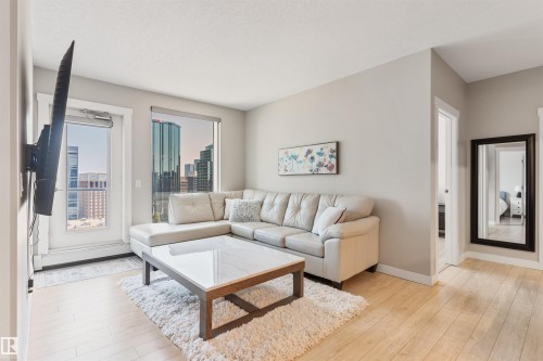 Living area featuring light wood-finish flooring, a full-height window with city buildings visible, and a white framed door - #2205 10226 104 St Nw, Edmonton, AB - Indoor Photo Showing Living Room