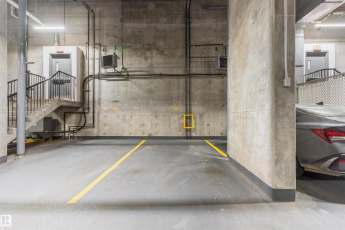 Concrete parking area featuring marked spaces, a concrete staircase with metal railings, and a secured door with an exit sign - #2205 10226 104 St Nw, Edmonton, AB - Indoor Photo Showing Garage