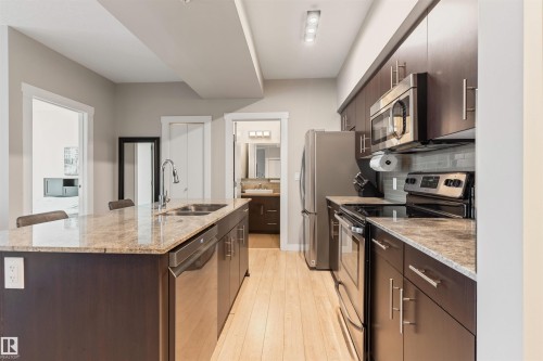 Kitchen featuring an island with stone countertop and undermount sink, stainless steel appliances, dark wood cabinetry, and light wood-finish flooring - #2205 10226 104 St Nw, Edmonton, AB - Indoor Photo Showing Kitchen With Double Sink With Upgraded Kitchen