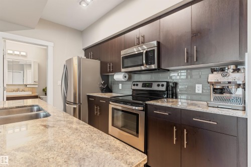 Kitchen featuring wood-finish cabinetry, stainless steel appliances, granite countertops, and a gray subway tile backsplash - #2205 10226 104 St Nw, Edmonton, AB - Indoor Photo Showing Kitchen With Double Sink