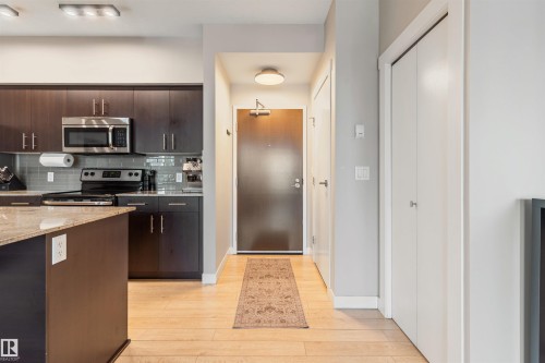 Open-concept kitchen with dark wood cabinetry, stainless steel appliances, and a light-toned granite island - #2205 10226 104 St Nw, Edmonton, AB - Indoor Photo Showing Kitchen
