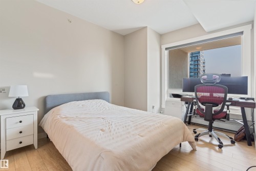 Light-toned wood-finish flooring complements neutral wall paint in this room featuring a large window - #2205 10226 104 St Nw, Edmonton, AB - Indoor Photo Showing Bedroom