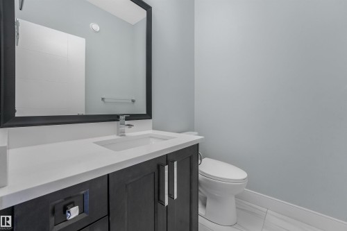 Bathroom featuring a dark wood-finish vanity with a white countertop, an integrated rectangular sink, a chrome faucet, and a framed mirror - 6453 177A Avenue Nw, Edmonton, AB 