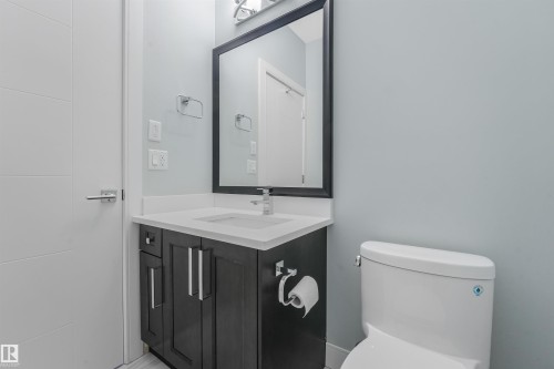 Bathroom featuring a dark wood-finish vanity with a white countertop, an undermount sink, a framed mirror, and a modern toilet - 6453 177A Avenue Nw, Edmonton, AB 