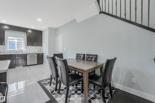Kitchen with dark wood-finish cabinetry, stainless steel dishwasher, mosaic tile backsplash, and light-toned tile flooring - 6453 177A Avenue Nw, Edmonton, AB 
