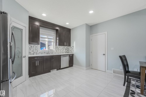 Contemporary kitchen featuring dark wood-finish cabinetry, stainless steel appliances, and a mosaic tile backsplash - 6453 177A Avenue Nw, Edmonton, AB 