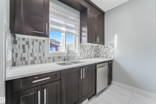 Dark wood-finish cabinetry, white countertops, mosaic tile backsplash, stainless steel sink, and stainless steel dishwasher - 6453 177A Avenue Nw, Edmonton, AB 