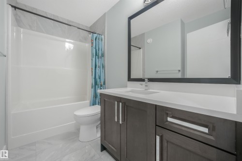 White subway tile shower surround with a built-in tub, dark wood-finish vanity with a white countertop, and a large framed mirror - 6453 177A Avenue Nw, Edmonton, AB 