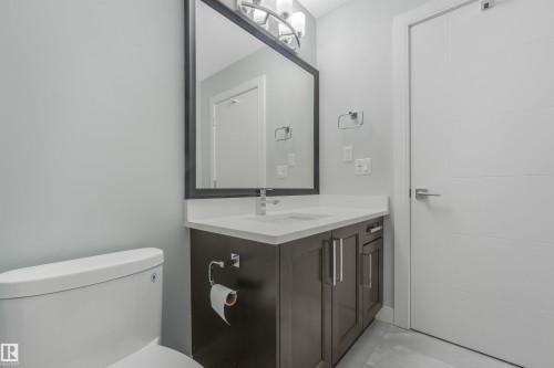 Contemporary vanity with a white countertop and integrated sink, dark wood-finish cabinetry, a framed mirror, and modern light fixtures - 6453 177A Avenue Nw, Edmonton, AB 