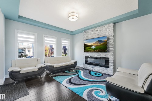 Tray ceiling with accent color, stone-clad fireplace feature wall, built-in electric fireplace, recessed lighting, and dark wood-finish flooring - 6453 177A Avenue Nw, Edmonton, AB 