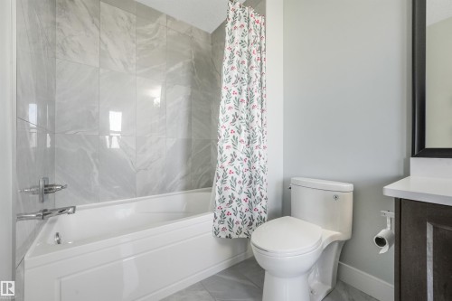 Full bath featuring a tub-shower combination with floor-to-ceiling tile surround, a single toilet, and a vanity with a white countertop - 6453 177A Avenue Nw, Edmonton, AB 