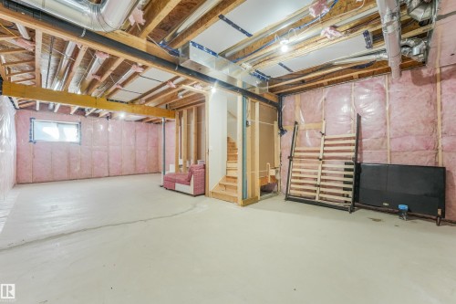 Unfinished lower level with exposed ceiling joists, insulation, a window, and wood stairs - 6453 177A Avenue Nw, Edmonton, AB 