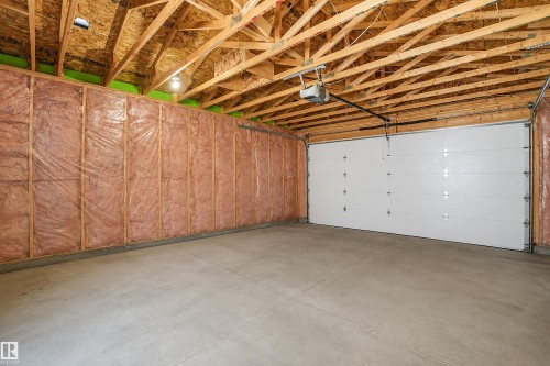 Exposed wood rafters and ceiling joists with a white garage door, concrete floor, and insulation - 6453 177A Avenue Nw, Edmonton, AB 