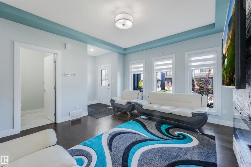 Recessed ceiling with accent paint, dark wood-finish flooring, multiple windows with blinds, and a built-in stone-clad media wall - 6453 177A Avenue Nw, Edmonton, AB 