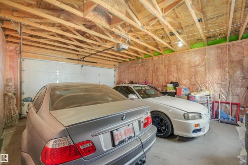 Unfinished garage featuring exposed wooden trusses, concrete flooring, and an overhead garage door - 6453 177A Avenue Nw, Edmonton, AB 